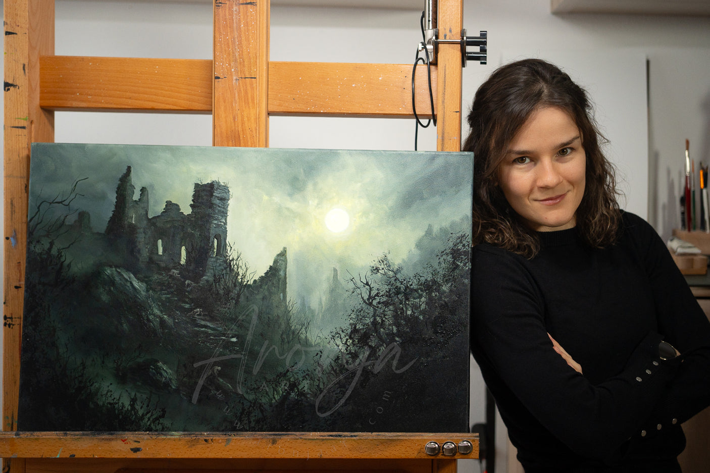 Woman standing beside a hand-painted traditional fantasy landscape depicting a dark castle ruin under a pale moon, showcasing the SORCERY Gothic Original Painting "Silent Hill" - 60x40cm / Acrylics, fantasy artist style.