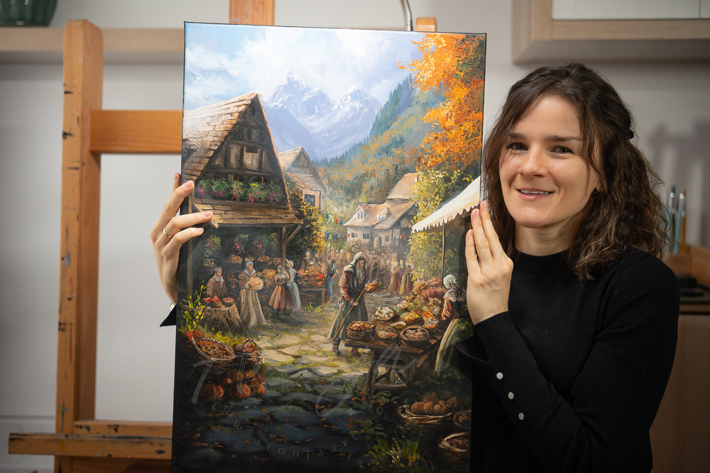Woman holding SORCERY Gothic Original Painting "Harvest Festival" - 60x40cm / Acrylics depicting a detailed autumn village scene with market stalls, villagers, flower baskets, and mountainous landscape in the background, hand-painted fantasy art inspired by traditional and gaming themes.