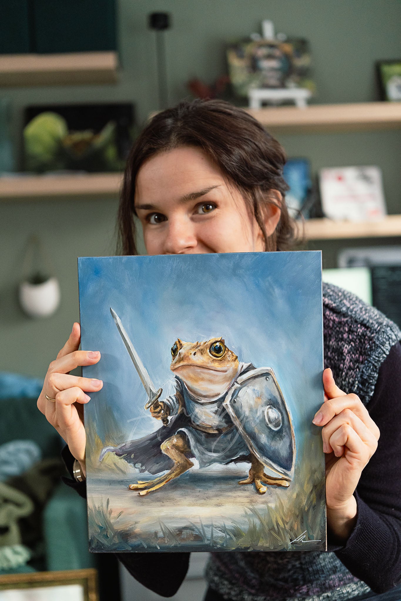 Woman holding "Toad Warrior - oil painting" depicting a detailed fantasy animal character with sword and shield, showcasing original hand-painted oil artwork inspired by gaming and nature.