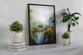 The Valley Of Imladris - Print showing a detailed fantasy landscape with waterfalls, lush greenery, and medieval-style buildings framed and displayed on a shelf with decorative plants.