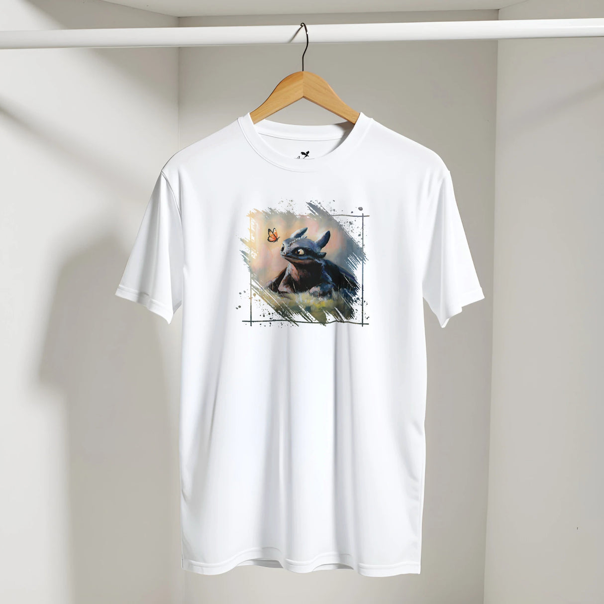 White Toothless T-shirt featuring a fantasy art design of a small black dragon with wings looking at a glowing butterfly, displayed on a wooden hanger.